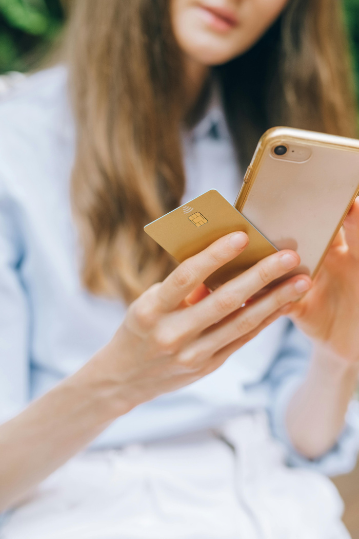 Essential Credit Union - a woman on her phone with a debit card in her hand