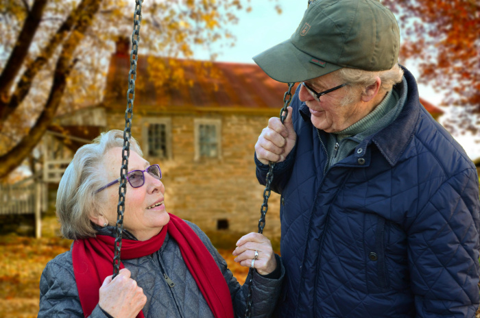 a senior couple chatting while sitting on a swing set outside discussing senior chekcing accounts in walker la
