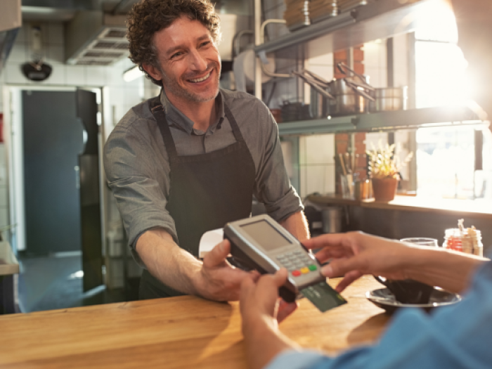 aa cafe owner smiling processing a transaction with a customer using their simple checking account from Essential Credit Union in Houston