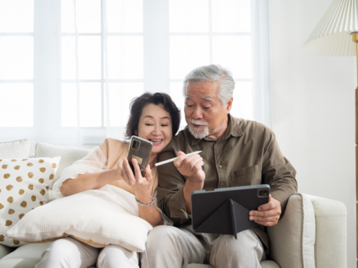 a senior couple sitting on the couch looking at their devices excitedly as they view their prosperity rewards checking account from Essential Credit Union in Houston