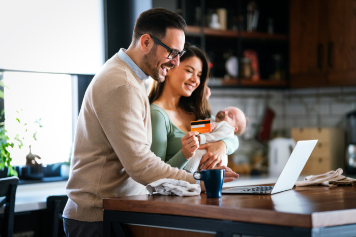 a young vcouple holding a baby in their kitchen as they browse personal loan options with essential credit union in walker