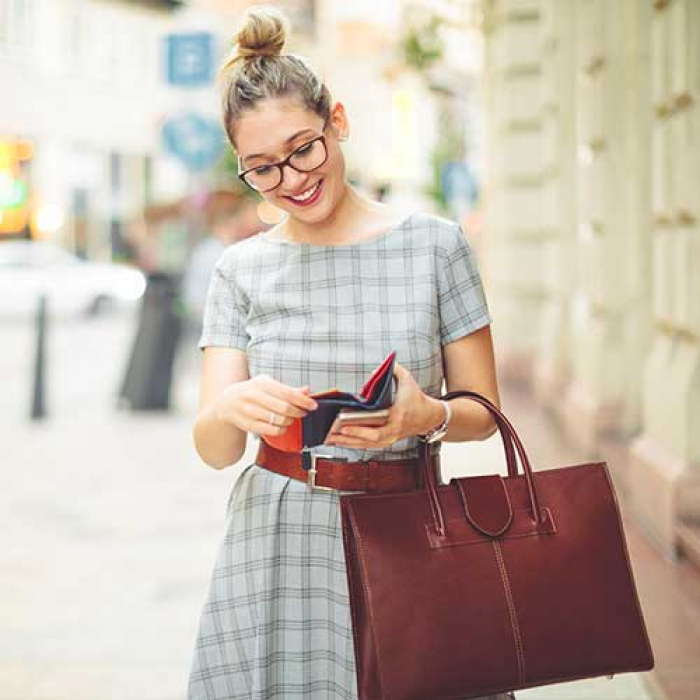 Woman smiling at her wallet while holding a red handbag