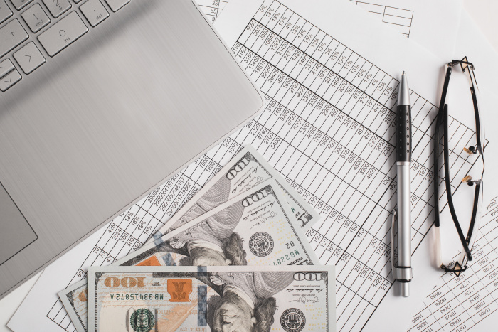 a laptop and cash sitting on top of a stack of papers containing share certificate rates